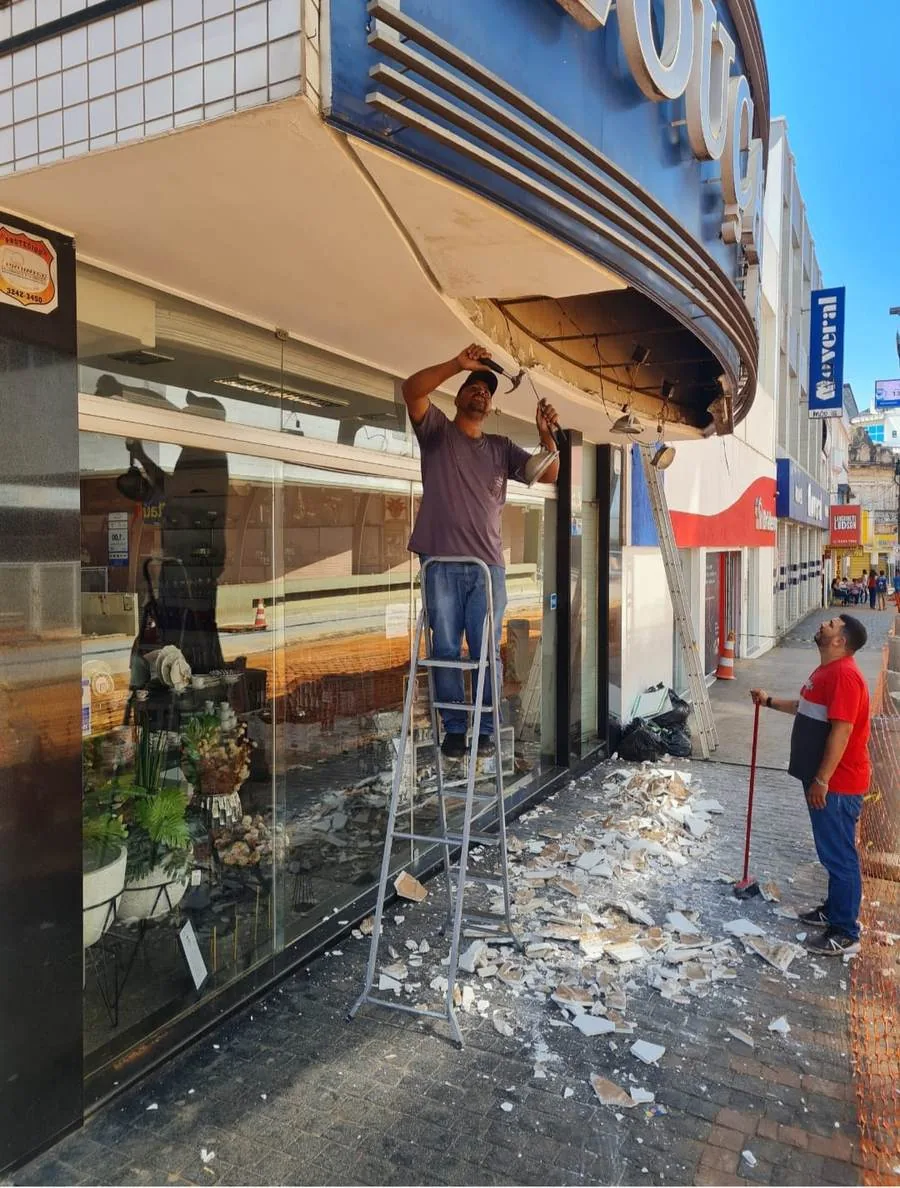 Operário com martelo na mão sobre o letreiro antigo, no meio da obra de troca da fachada da loja