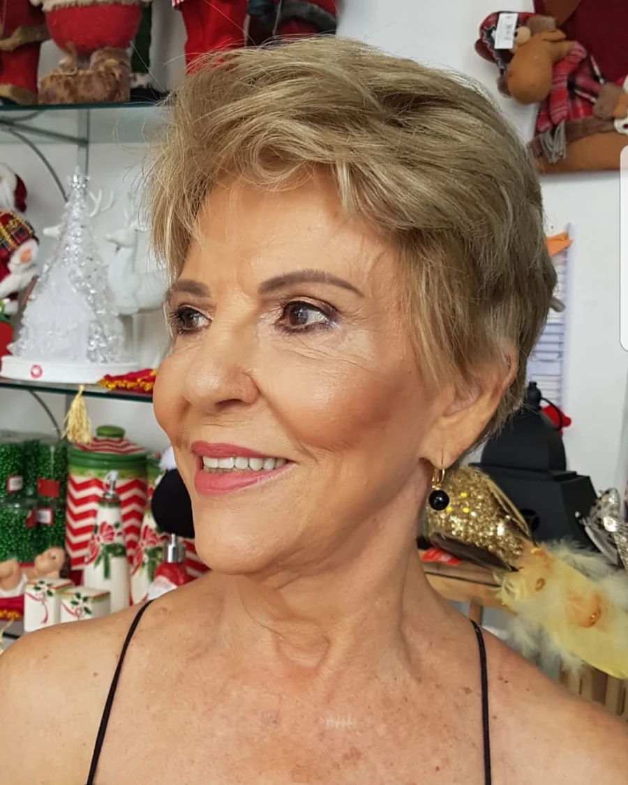 Dona Fátima sorrindo dentro da loja, de perfil, com as prateleiras de Natal ao fundo