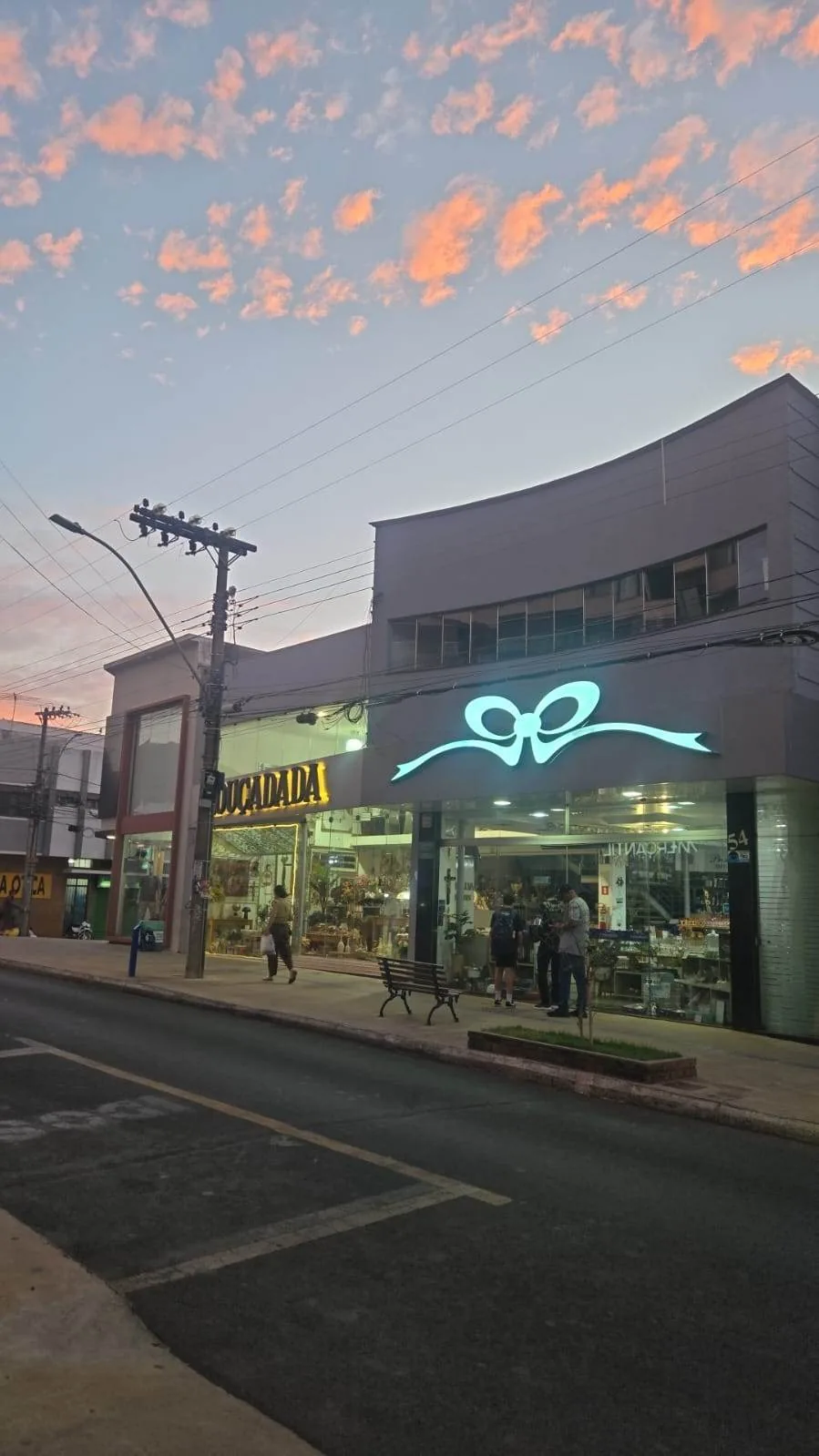 O laço da Louçadada aceso em azul na fachada, no entardecer, com o céu rosa ao fundo