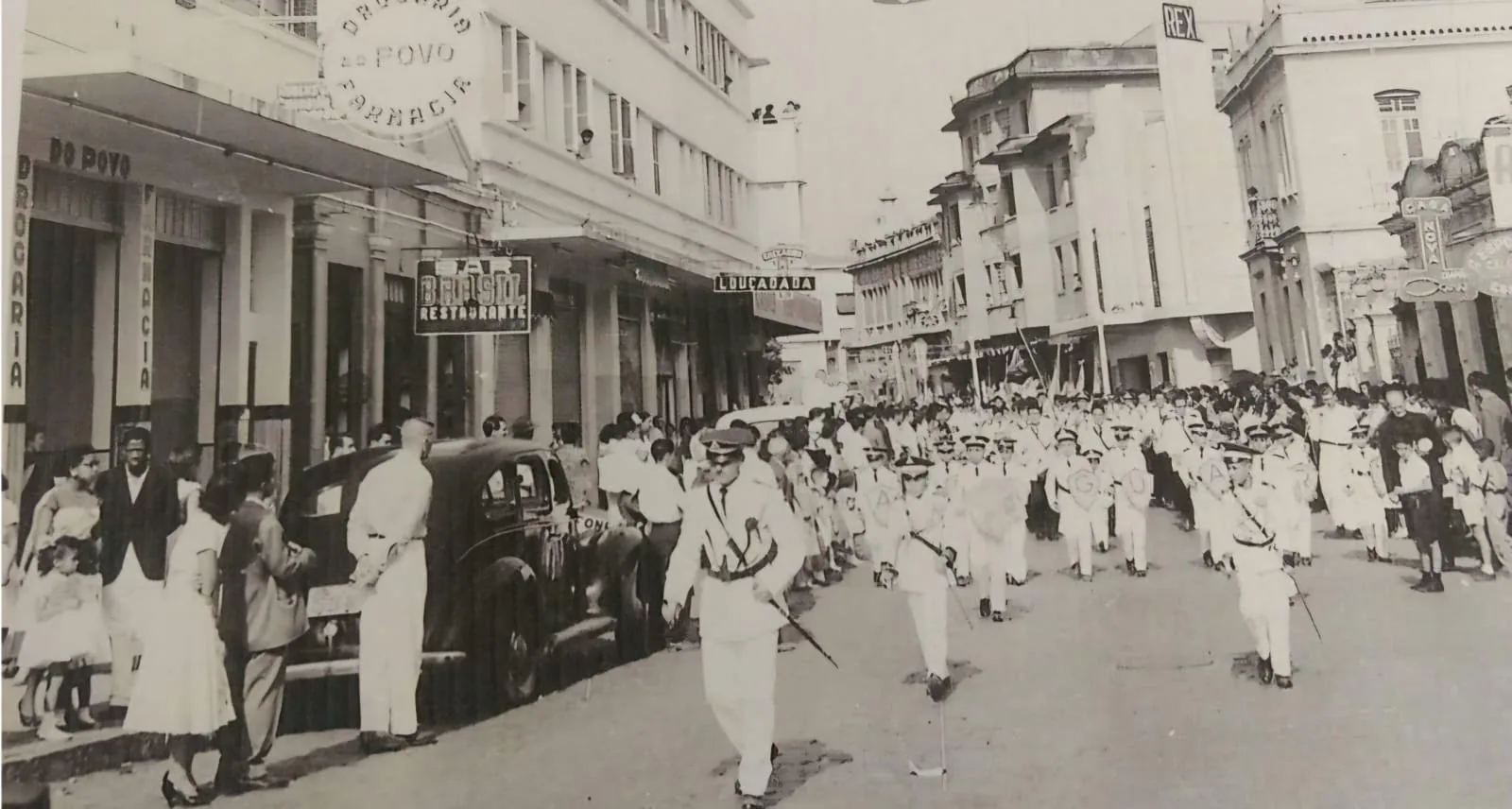 Fotografia antiga da rua do centro de Araguari em dia de festa, tomada por gente e bandeirinhas entre as fachadas